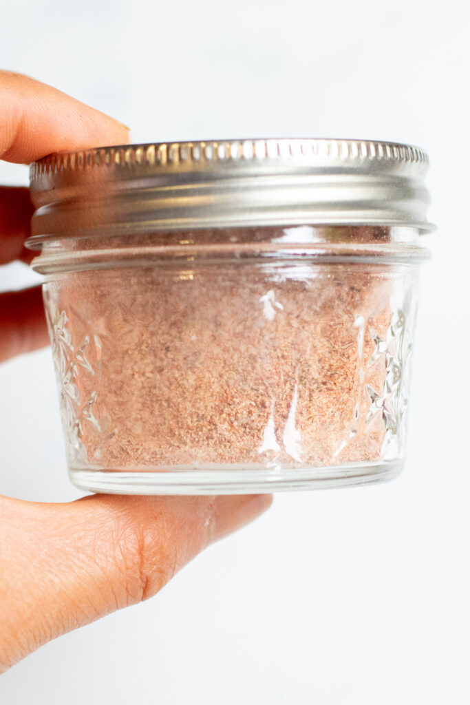 a hand holding a small mason jar with spice blend.