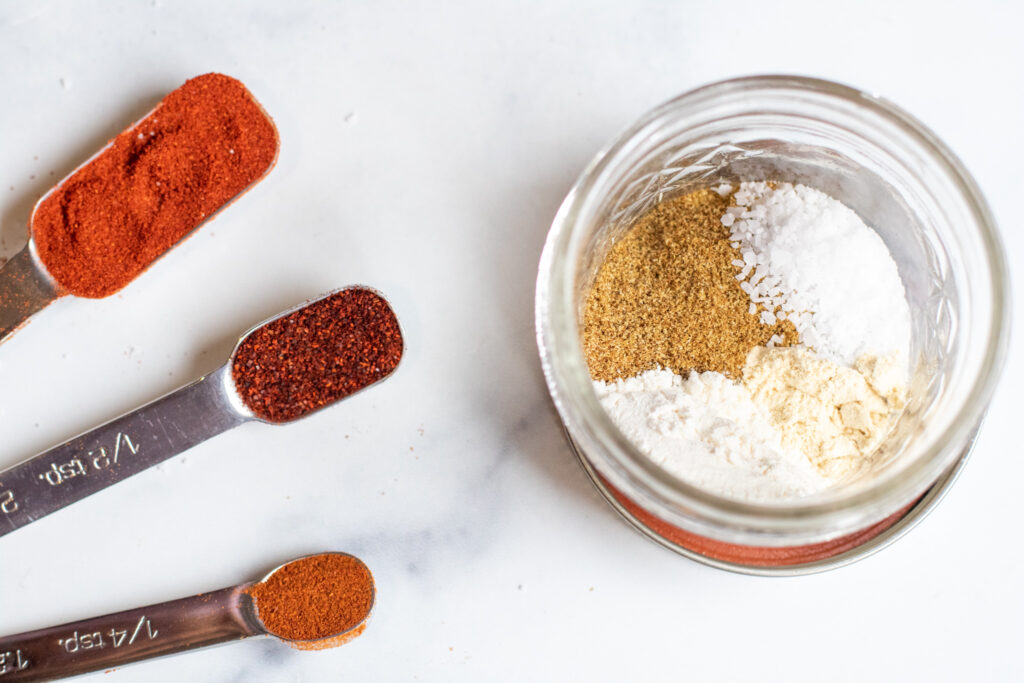 measuring spoons with spices and an open small mason jar.