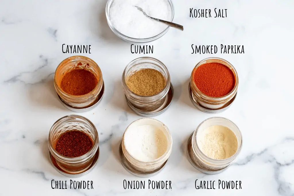 small jars of open spices and salt on a counter.