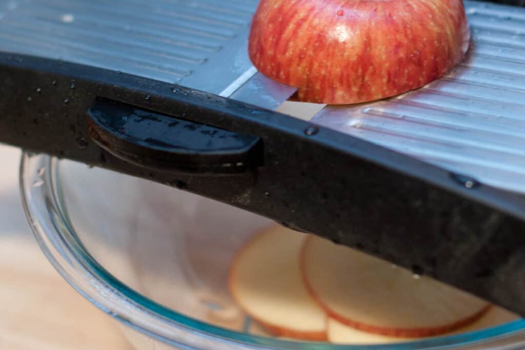 an apple being sliced on a mandoline.