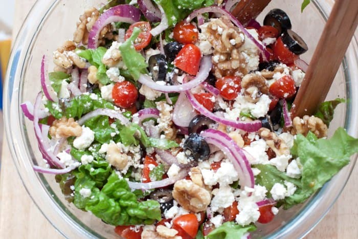 Greek-ish salad in a large bowl with tongs