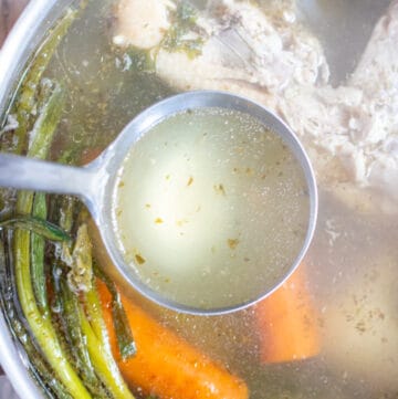 a spoon ladle with some stock from a pot with chicken and veggies.