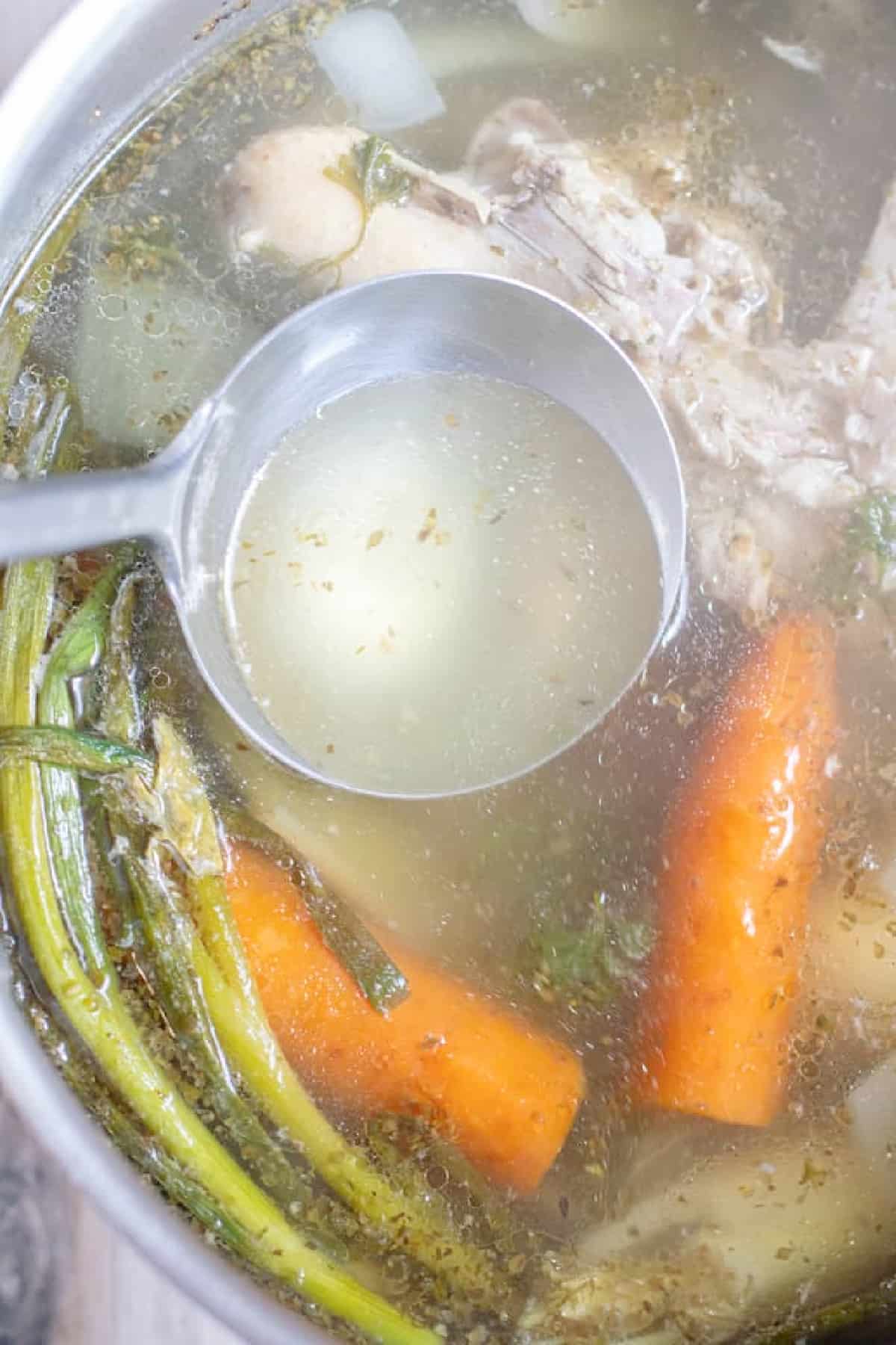 a ladle of stock over a pot of chicken and veggies.