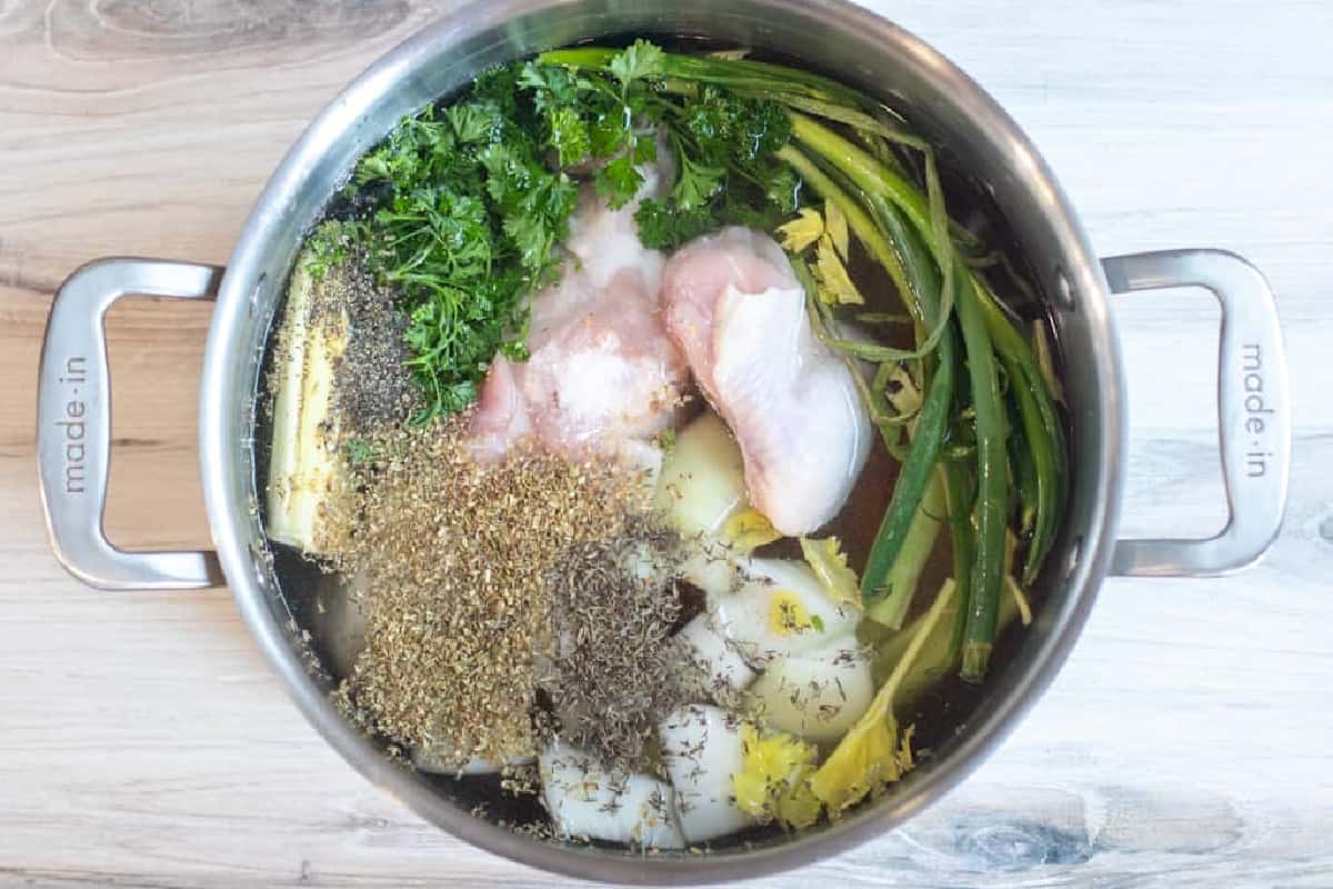 a pot of veggies and raw chicken and herbs.