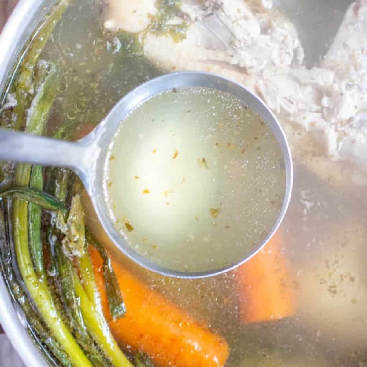 a ladle of stock over a pot of chicken and veggies.