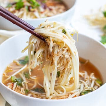 a bowl of chicken pho with chopstick holding up noodles and chicken.