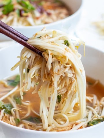 a bowl of chicken pho with chopstick holding up noodles and chicken with Pinterest pin text.