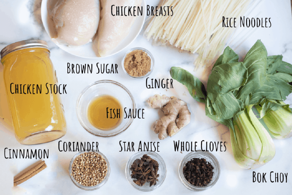 chicken stock, raw chicken, rice noodles, bok choy, fish sauce, brown sugar, ginger, coriander, star anise, whole cloves, cinnamon stick on a counter.