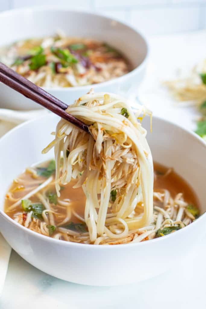 a bowl of chicken pho with chopstick holding up noodles and chicken.