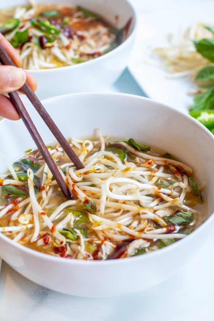 overhead of two bowls of chicken pho with chopsticks.