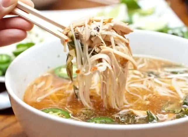large bowl of pho with chopsticks holding up a bite