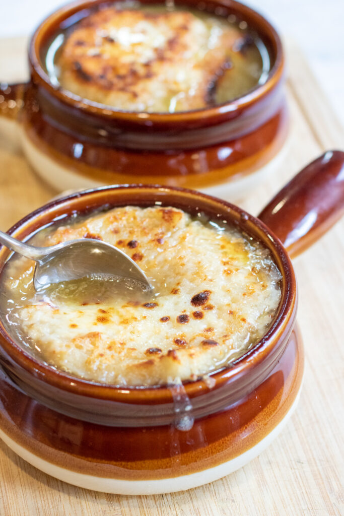 crocks of soup with melted cheese and a spoon