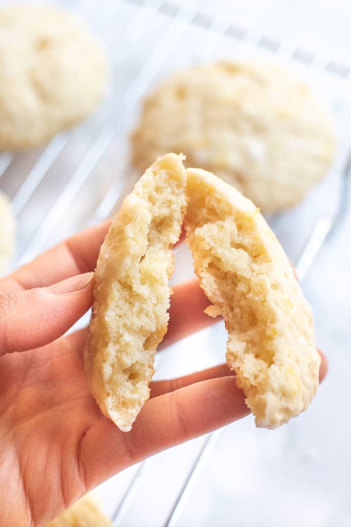 a hand holding a lemon cookie in half.