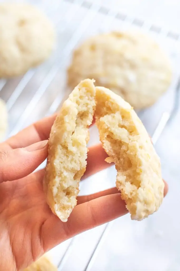 a hand holding a lemon cookie in half.