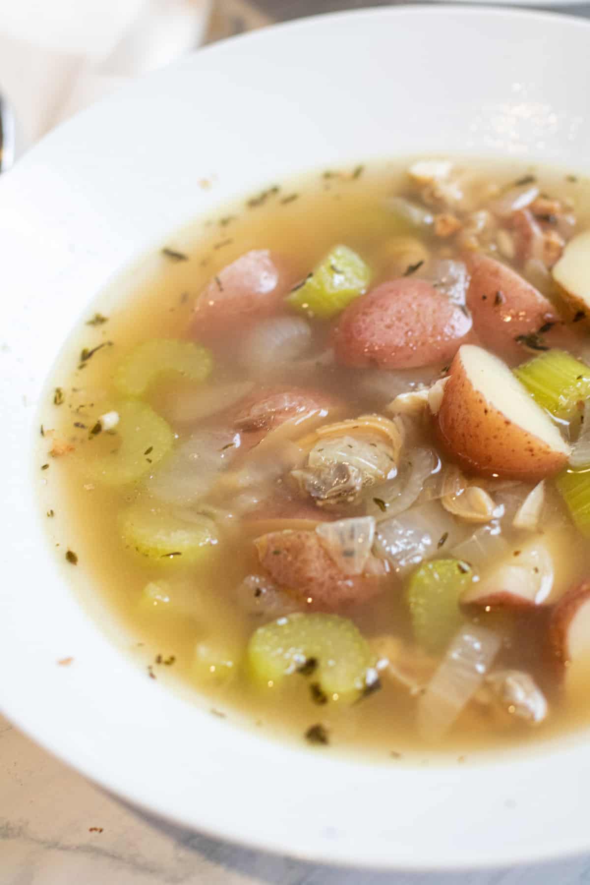 a bowl of clear chowder with clams and potatoes.