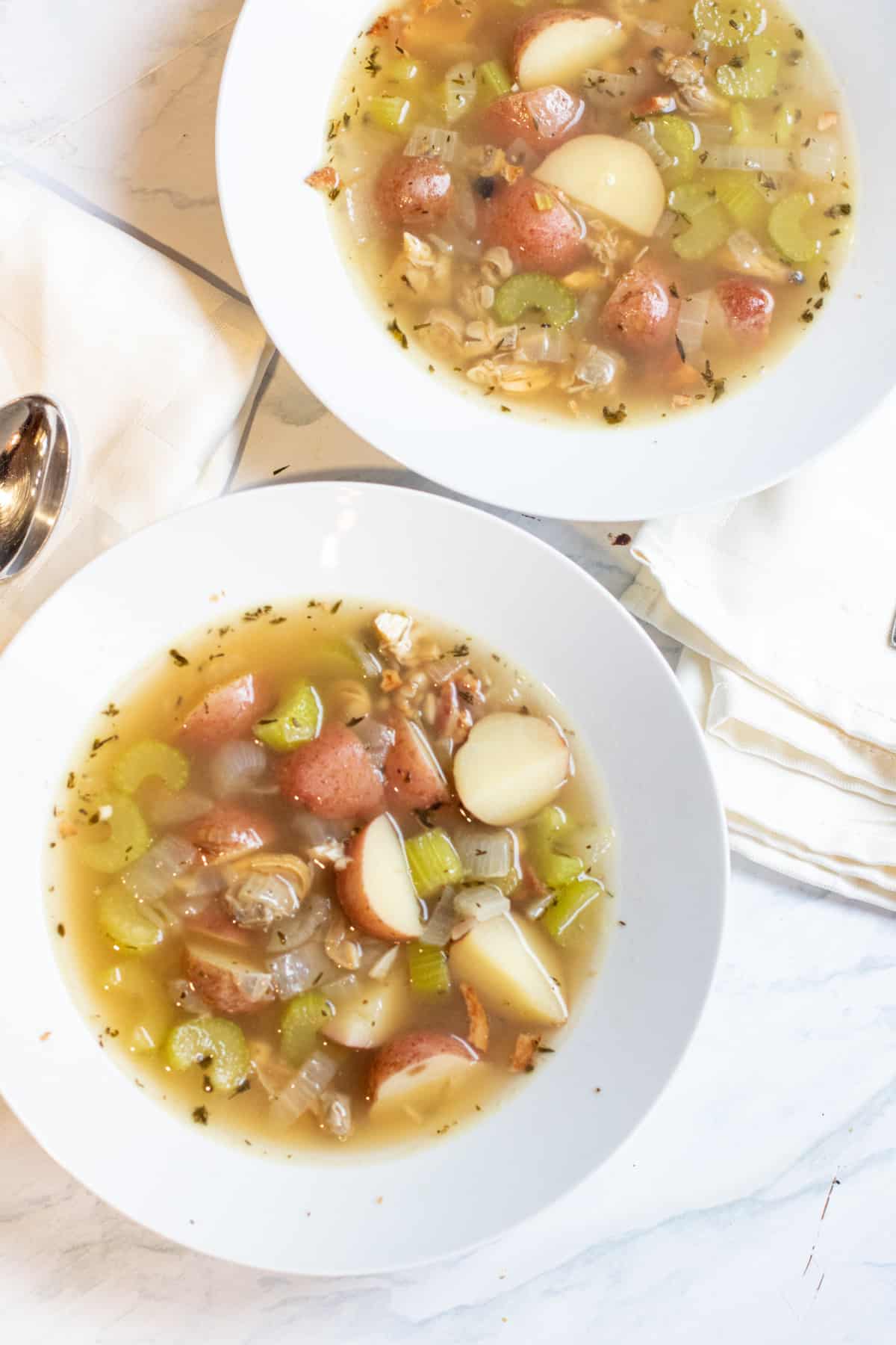 a bowl of clear chowder with clams and potatoes.