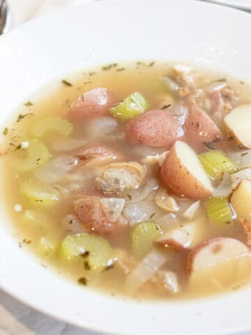 a bowl of clear chowder with clams and potatoes.