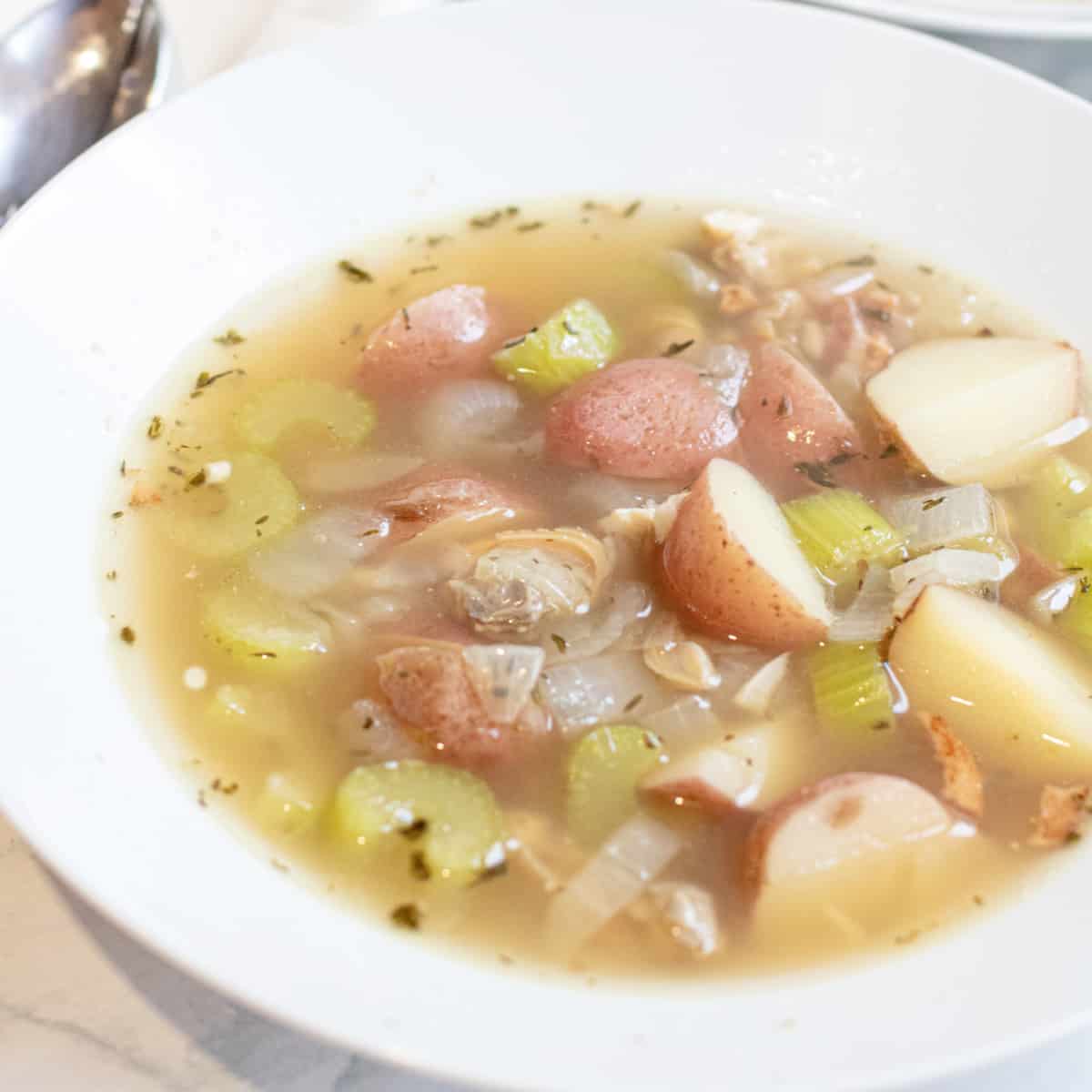 a bowl of clear chowder with clams and potatoes.