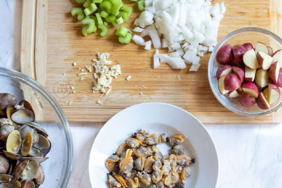 chopped celery and onions and potatoes, clams and garlic on counter.