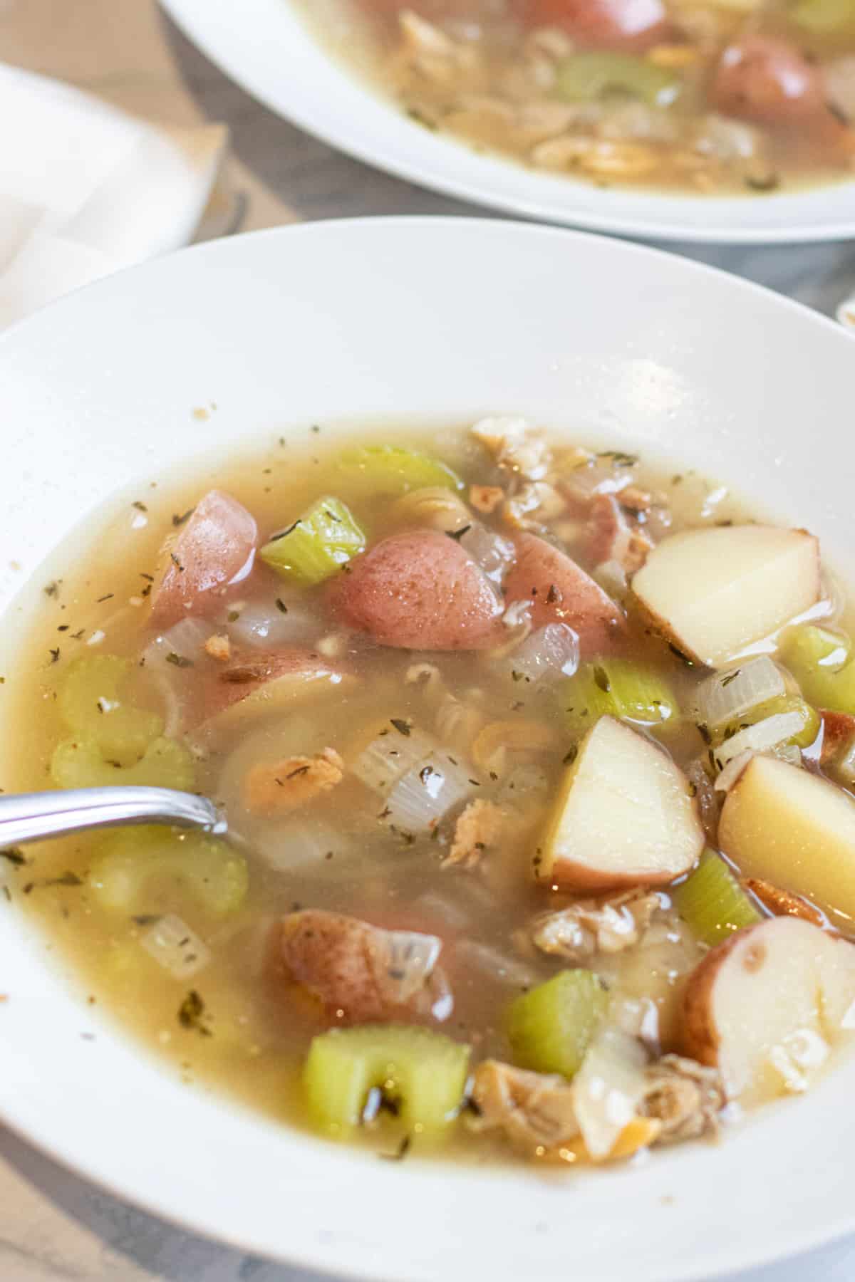 a bowl of clear chowder with clams and potatoes.