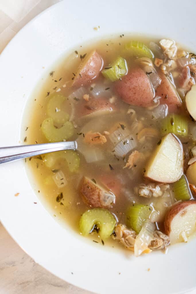 a bowl of clear chowder with clams and potatoes.