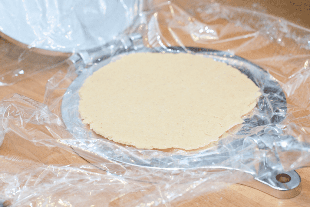 a flattened corn tortilla in plastic wrap in an open tortilla press.