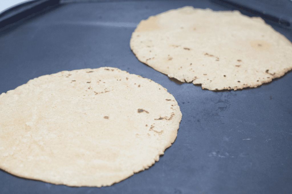 corn tortillas being cooked on a griddle.