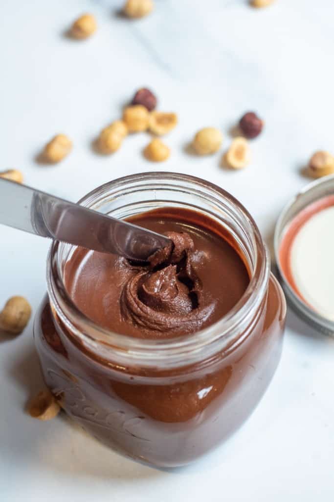 an open jar of nutella with a knife in it.