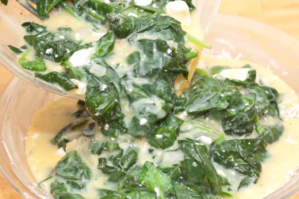 sauteed spinach, feta, and eggs being poured into a pie dish.