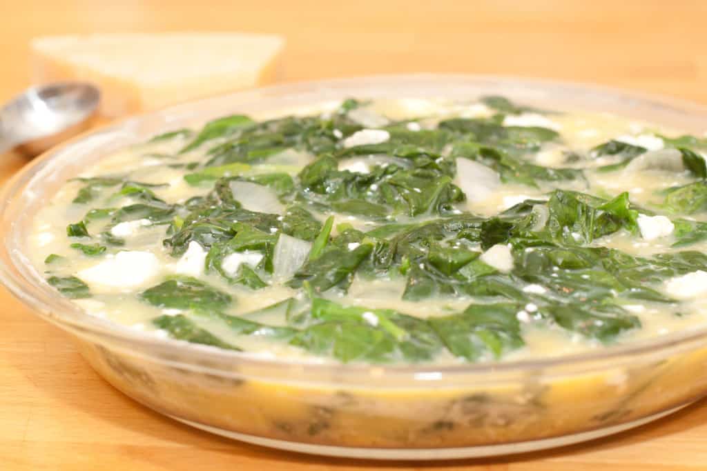 a pie dish of uncooked spinach quiche.