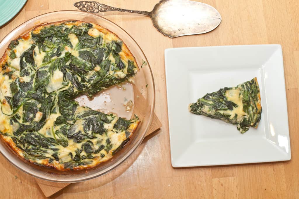 a pie plate with baked spinach quiche and a plate with a slice of quiche.