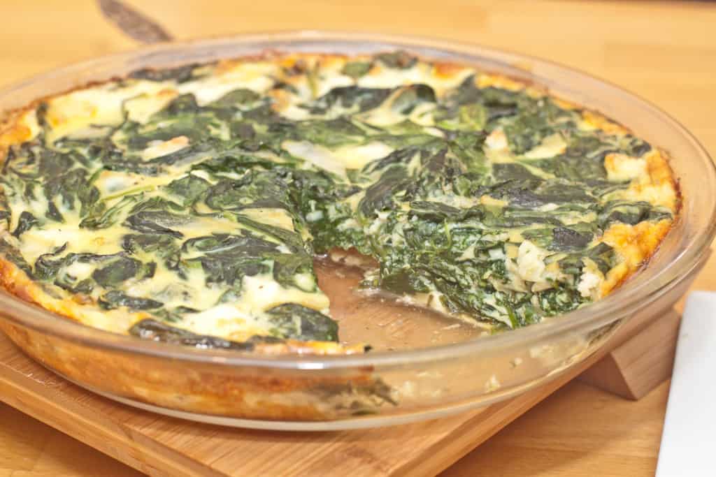 a pie dish of spinach quiche with a slice taken out.