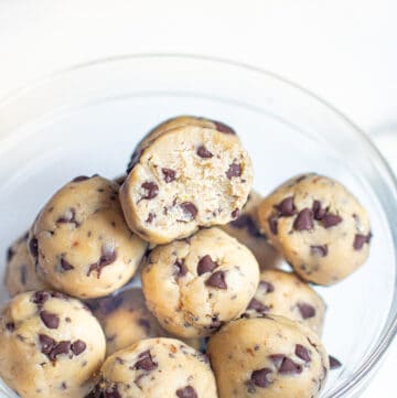 a bowl of cookie dough balls with one with a bite taken out.