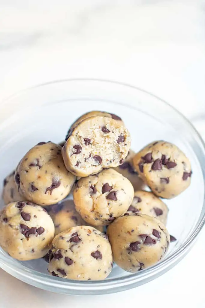 a bowl of cookie dough balls with one with a bite taken out.