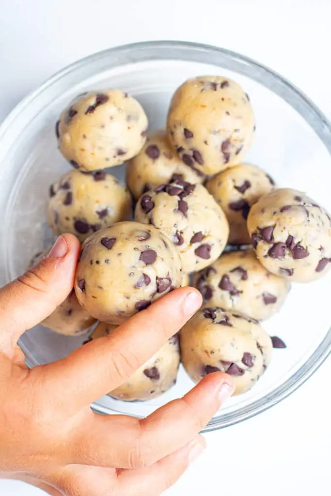 a bowl of cookie dough balls with a hand grabbing one.