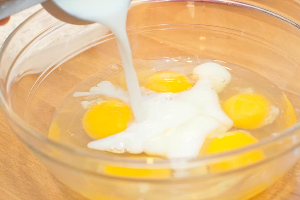 a large bowl with eggs and milk being poured in.
