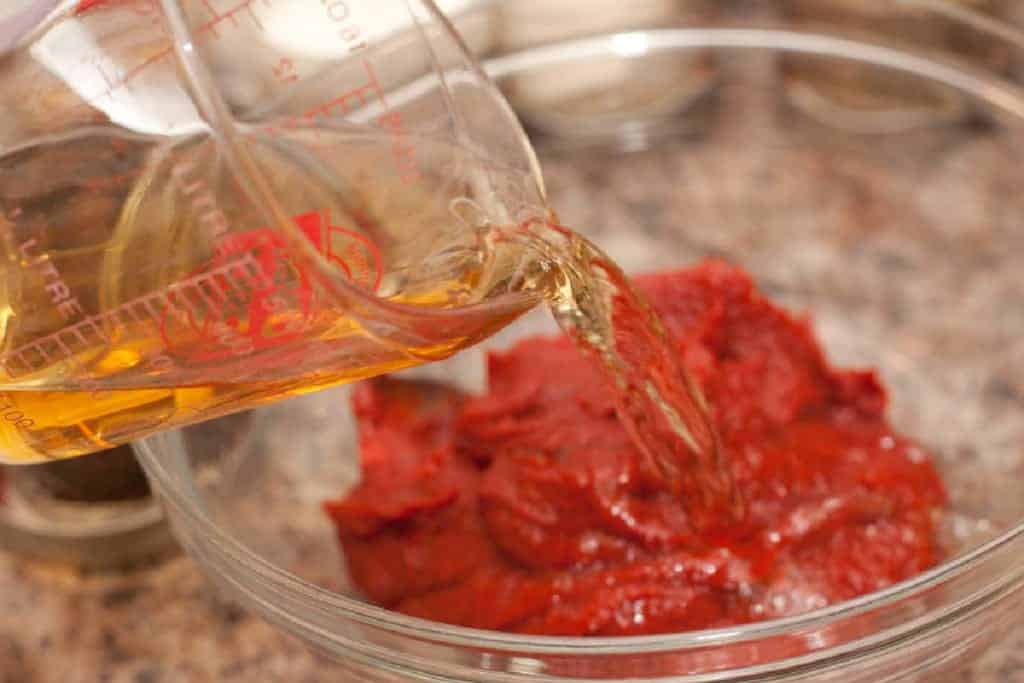 pouring vinegar into a bowl of tomato paste.