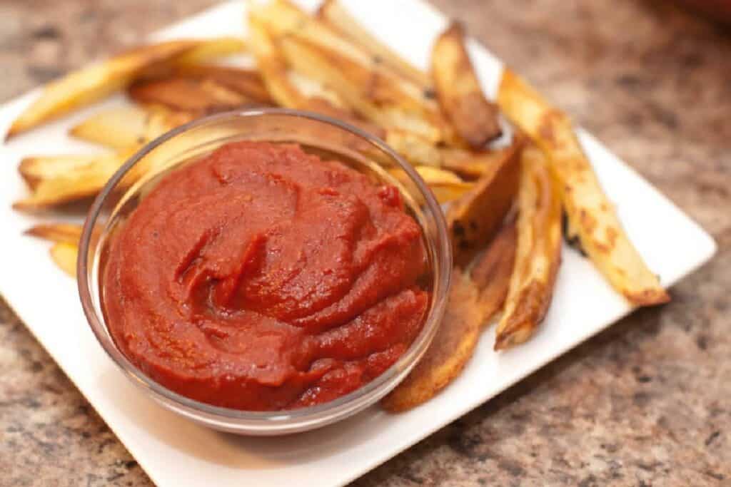 a close up of a small bowl of ketchup on a plate of fries.