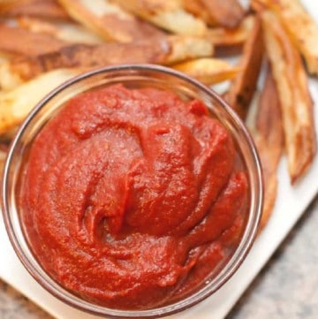 a close up of a small bowl of ketchup on a plate of fries.