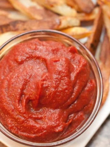 a close up of a small bowl of ketchup on a plate of fries.