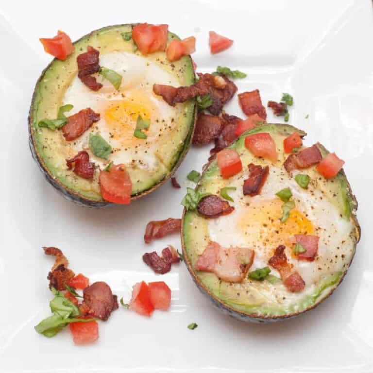 an overhead of a halved avocado with eggs baked in topped with tomatoes and bacon.