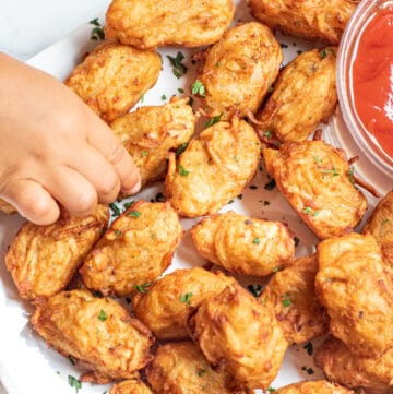 a plate of homemade tater tots with ketchup and a little hand grabbing one.