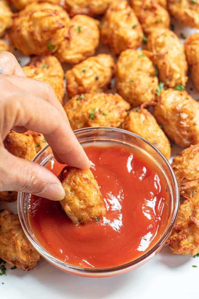 a hand dunking a tater tot in ketchup.