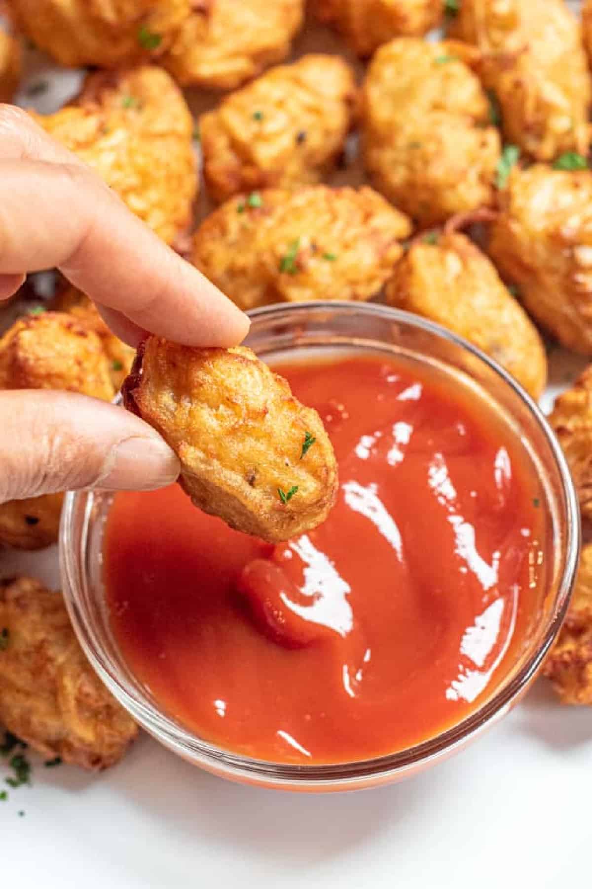 a hand holding up a tater tot with ketchup.