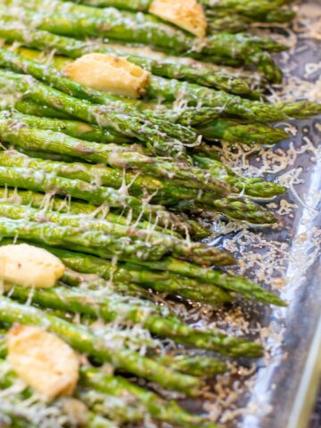 a pan of cooked asparagus with garlic and melted cheese.