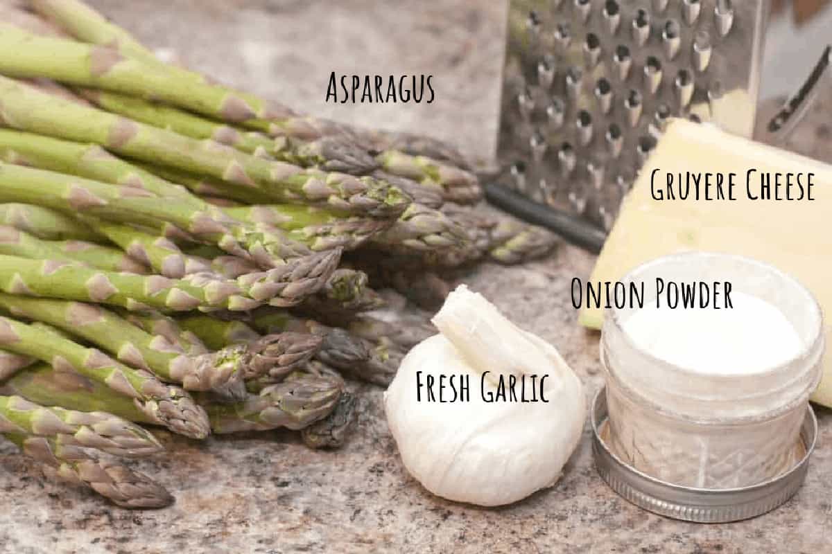 raw asparagus, garlic, onion powder, gruyere, and cheese grater on counter.