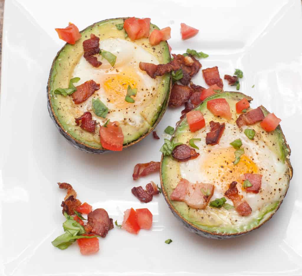 overhead of a halved avocado with eggs and crumbled bacon and tomatoes.