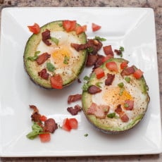 overhead of a halved avocado with eggs and crumbled bacon and tomatoes.