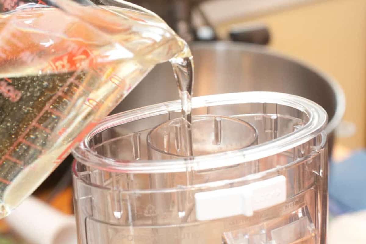 a Pyrex pouring oil into the to of a food processor.