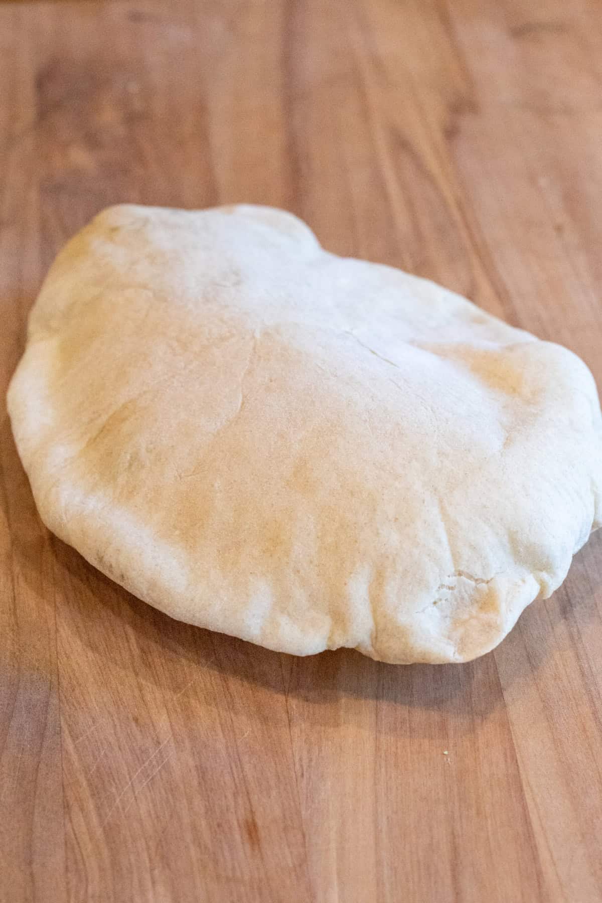 a baked uncut pita bread on a cutting board.